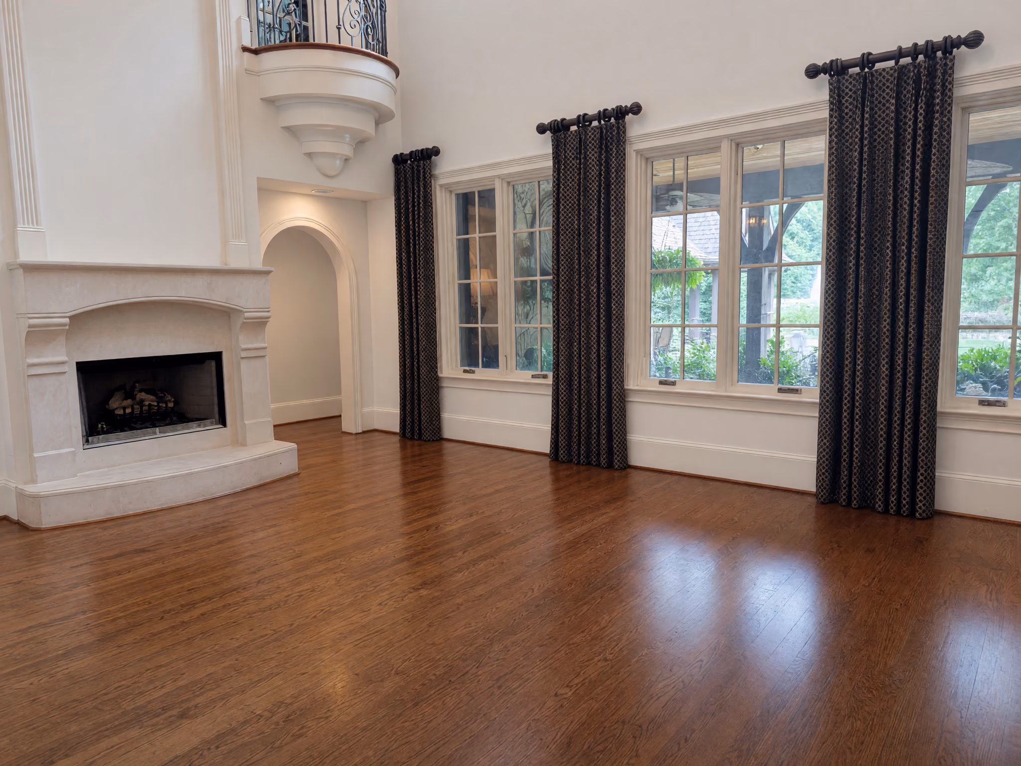 Virtually emptied double-height great room with fireplace and tall windows