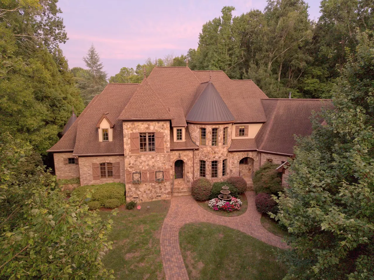 Aerial view of the stone facade, turreted roofline, brick paths and front garden fountain among trees